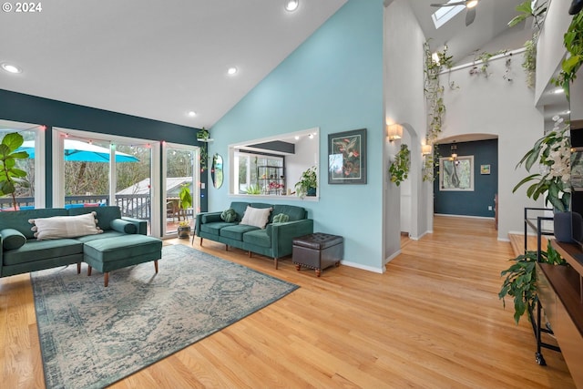 living room with light hardwood / wood-style flooring, high vaulted ceiling, a skylight, and ceiling fan