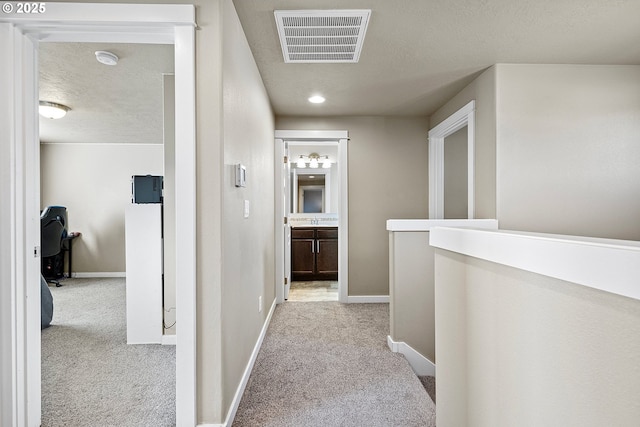 hall featuring a textured ceiling, carpet, visible vents, and baseboards