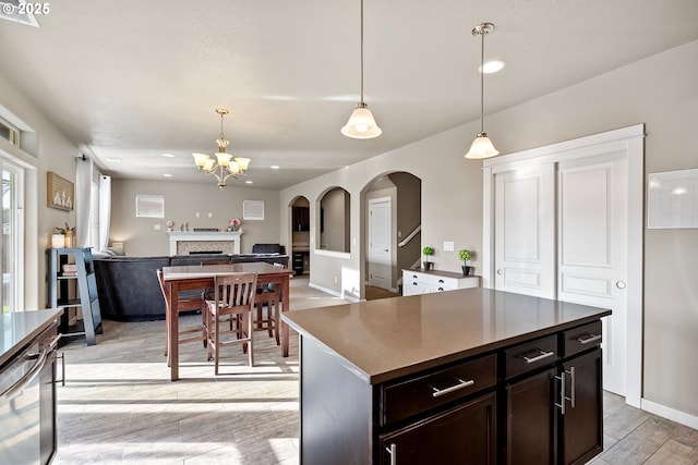 kitchen with light wood finished floors, a fireplace, arched walkways, pendant lighting, and open floor plan