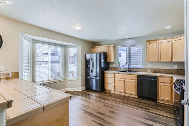 kitchen with sink, light brown cabinets, dark hardwood / wood-style floors, tile countertops, and black appliances