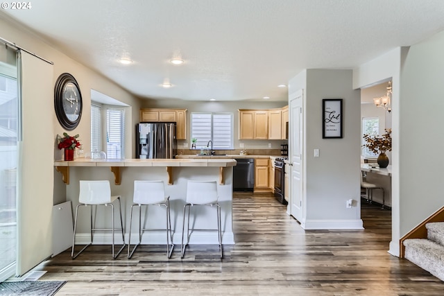 kitchen with tile counters, kitchen peninsula, a kitchen bar, black appliances, and hardwood / wood-style flooring