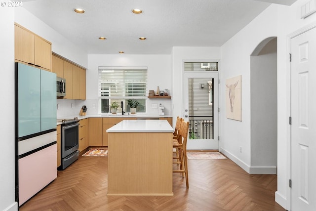 kitchen with stainless steel appliances, light brown cabinetry, sink, a kitchen island, and light parquet flooring