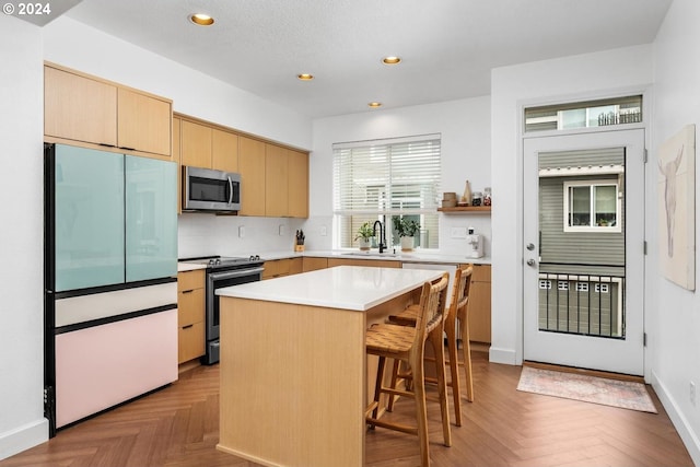 kitchen with stainless steel appliances, sink, a kitchen island, and light parquet floors