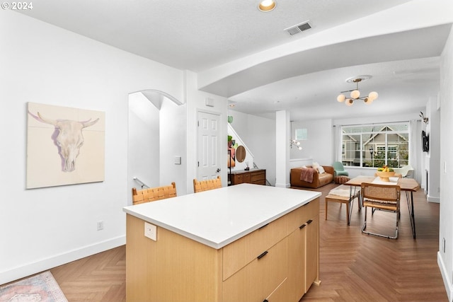 kitchen with a kitchen island, parquet floors, a chandelier, light brown cabinets, and a textured ceiling