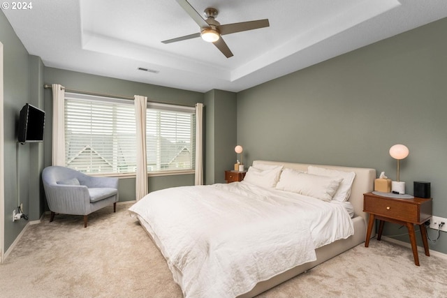 bedroom with a tray ceiling, light colored carpet, and ceiling fan