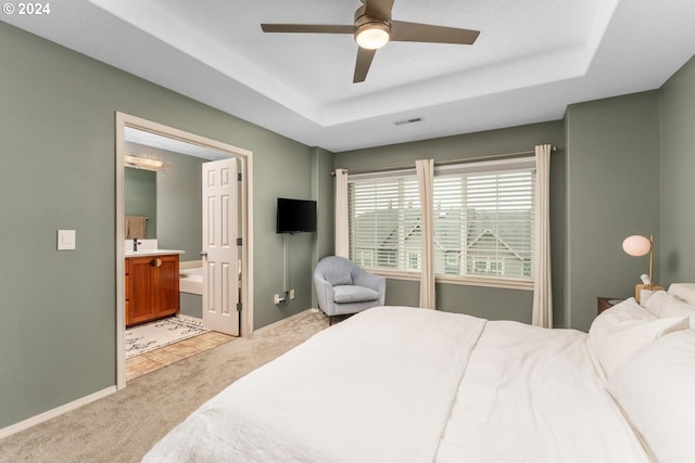 bedroom featuring ensuite bath, light colored carpet, a raised ceiling, and ceiling fan