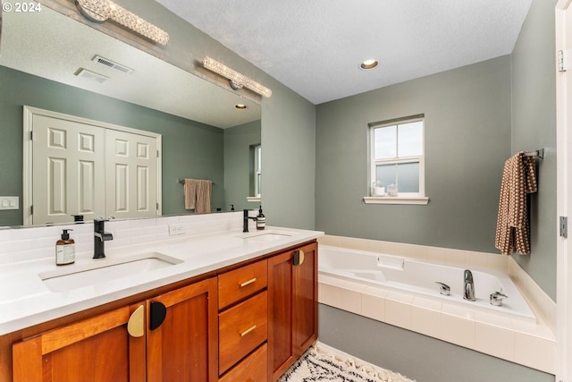 bathroom with vanity, a textured ceiling, and tiled tub