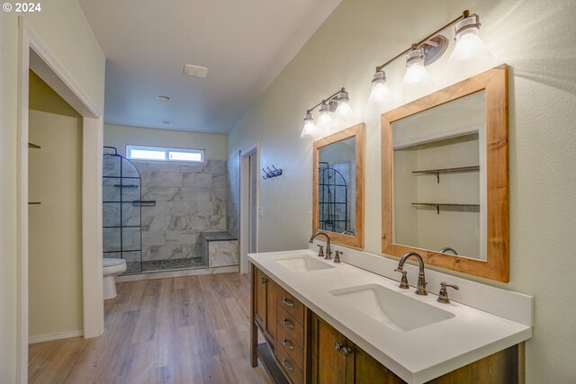 bathroom featuring hardwood / wood-style flooring, tiled shower, vanity, and toilet