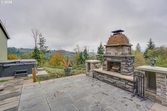 view of patio / terrace with a hot tub and an outdoor stone fireplace