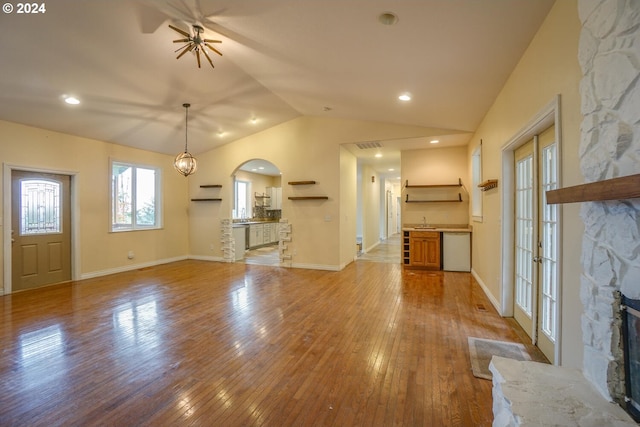 unfurnished living room featuring sink, hardwood / wood-style floors, a stone fireplace, and vaulted ceiling