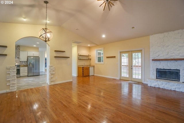 unfurnished living room with light wood-type flooring, vaulted ceiling, french doors, and a fireplace