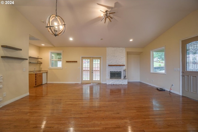 unfurnished living room with a stone fireplace, french doors, an inviting chandelier, dark wood-type flooring, and lofted ceiling