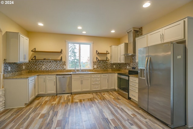 kitchen with appliances with stainless steel finishes, white cabinetry, wall chimney range hood, sink, and light hardwood / wood-style flooring