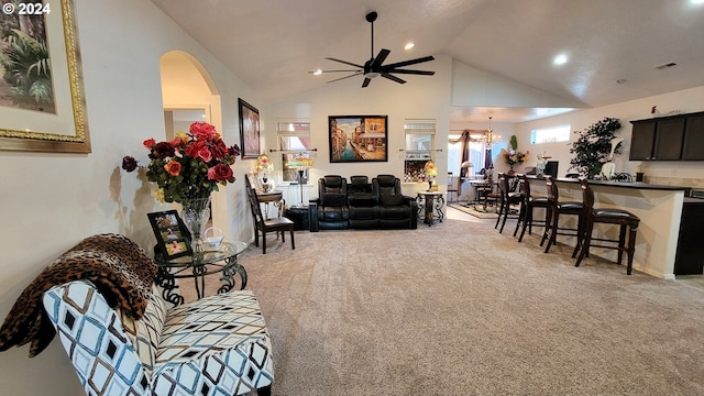 carpeted living room with ceiling fan with notable chandelier and high vaulted ceiling