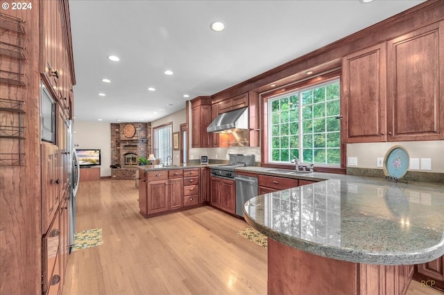 kitchen featuring kitchen peninsula, stainless steel appliances, sink, a brick fireplace, and light wood-type flooring