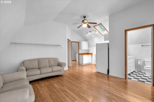 living room with lofted ceiling with skylight, light wood-type flooring, and ceiling fan