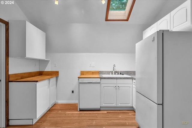 kitchen with white appliances, sink, vaulted ceiling with skylight, white cabinets, and light hardwood / wood-style flooring