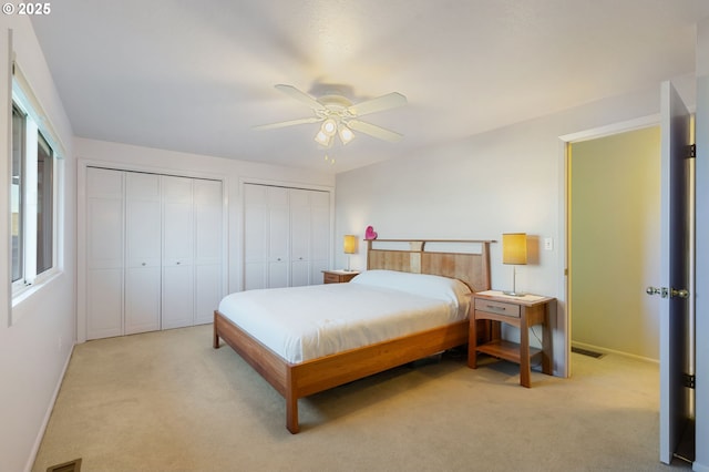 bedroom featuring two closets, ceiling fan, and light colored carpet