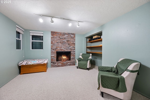 sitting room with carpet, track lighting, a textured ceiling, and a brick fireplace