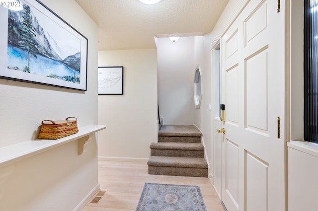 hallway with a textured ceiling and light hardwood / wood-style flooring