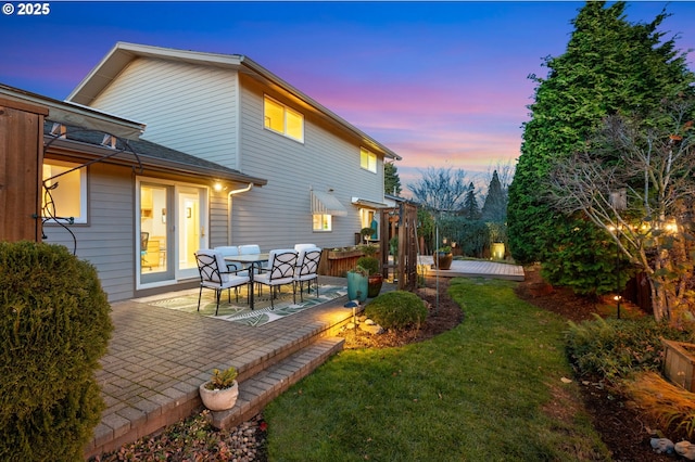 back house at dusk with a patio area and a yard