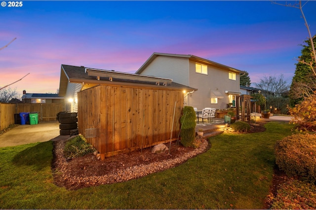 back house at dusk featuring a yard and a patio