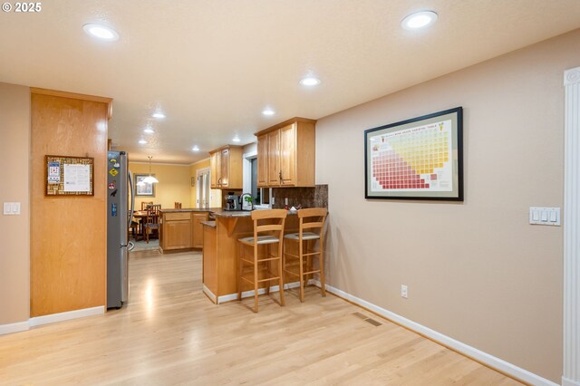 kitchen featuring kitchen peninsula, stainless steel fridge, pendant lighting, light hardwood / wood-style floors, and a breakfast bar area