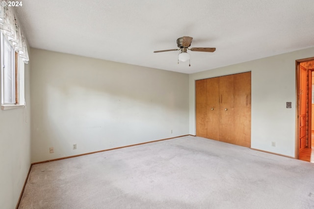 unfurnished bedroom featuring light carpet, a closet, ceiling fan, and a textured ceiling