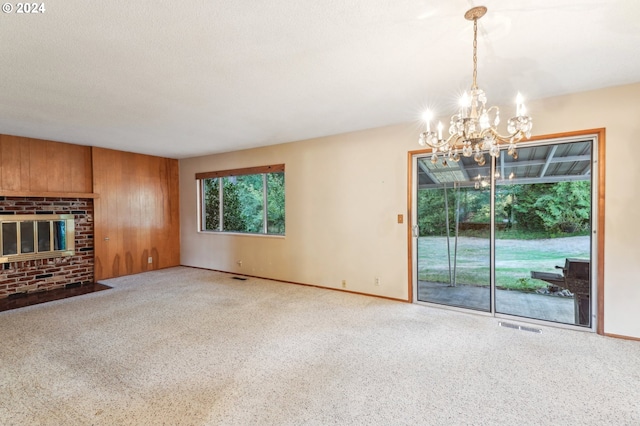 unfurnished living room featuring a notable chandelier, a brick fireplace, a textured ceiling, and carpet floors