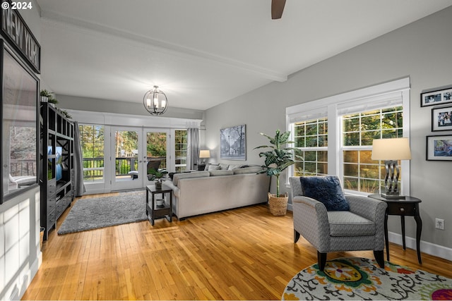 living room with beamed ceiling, ceiling fan with notable chandelier, light wood-type flooring, and french doors