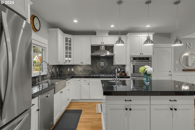 kitchen with pendant lighting, white cabinetry, a center island, stainless steel appliances, and wall chimney exhaust hood