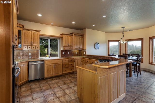 kitchen with hanging light fixtures, sink, appliances with stainless steel finishes, tasteful backsplash, and kitchen peninsula