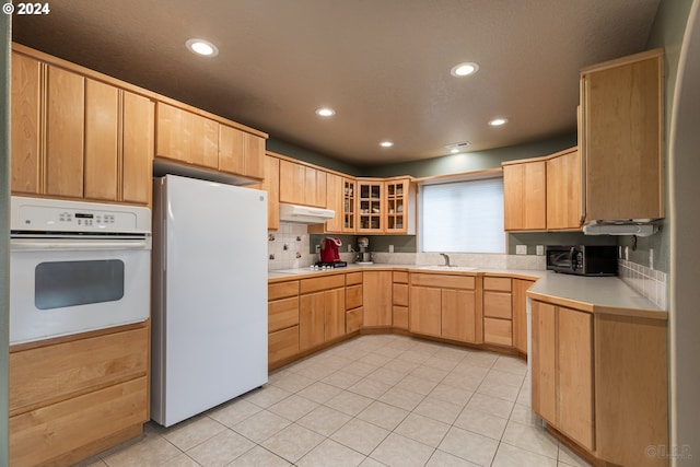 kitchen featuring decorative backsplash, light brown cabinetry, white appliances, sink, and light tile patterned floors