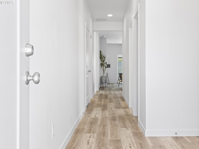 hallway with light wood-style flooring, visible vents, and baseboards