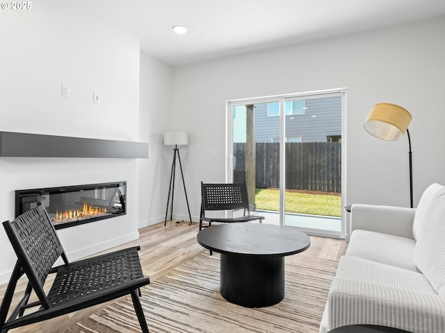 living area featuring light wood-style floors, recessed lighting, baseboards, and a glass covered fireplace