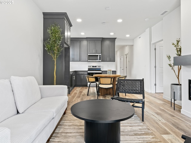 living area featuring baseboards, light wood-type flooring, visible vents, and recessed lighting