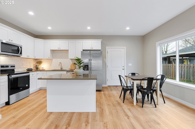 kitchen featuring white cabinets, a kitchen island, stainless steel appliances, light hardwood / wood-style floors, and sink