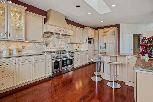 kitchen featuring custom exhaust hood, a skylight, light stone countertops, range with two ovens, and decorative backsplash