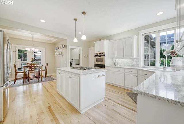 kitchen with hanging light fixtures, light hardwood / wood-style flooring, a kitchen island, white cabinetry, and stainless steel appliances