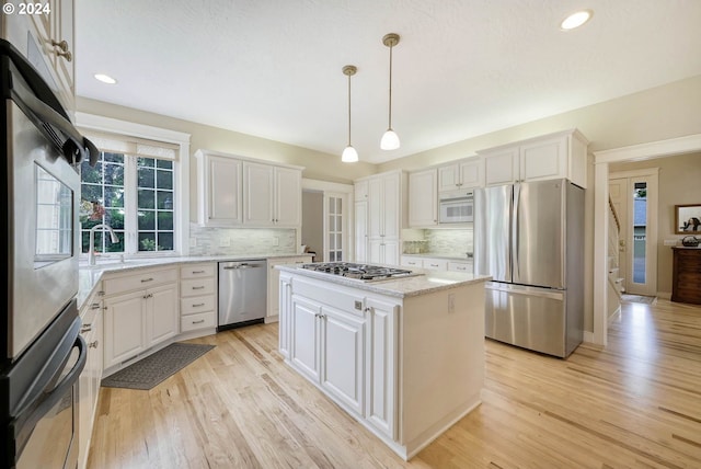 kitchen with white cabinetry, a center island, hanging light fixtures, stainless steel appliances, and light hardwood / wood-style flooring