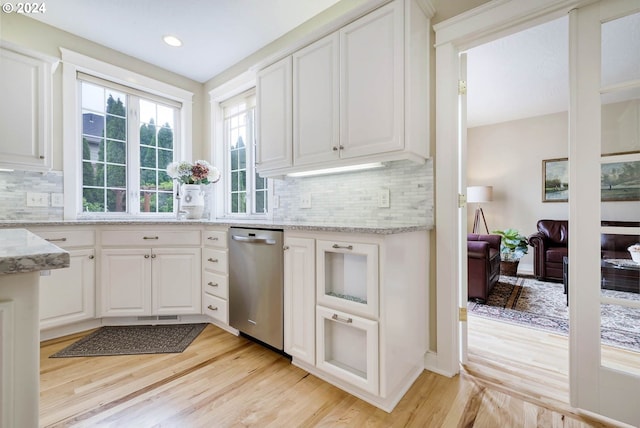 kitchen with white cabinetry, dishwasher, light stone countertops, light hardwood / wood-style flooring, and decorative backsplash