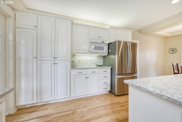 kitchen featuring light stone countertops, stainless steel fridge, light wood-type flooring, tasteful backsplash, and white cabinets