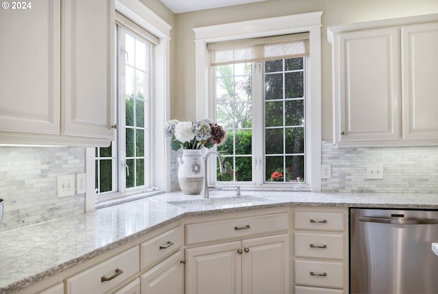 kitchen with light stone countertops, backsplash, stainless steel dishwasher, sink, and white cabinets