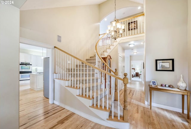 stairway with hardwood / wood-style floors, high vaulted ceiling, and a notable chandelier