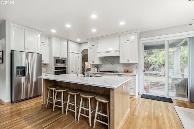 kitchen with white cabinets, appliances with stainless steel finishes, custom exhaust hood, and a kitchen island with sink