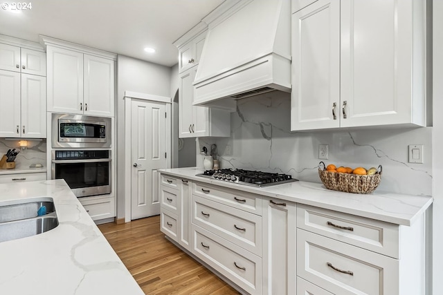 kitchen featuring premium range hood, white cabinetry, stainless steel appliances, and light wood-type flooring