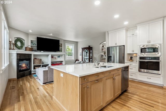 kitchen featuring appliances with stainless steel finishes, sink, a fireplace, white cabinetry, and a center island with sink