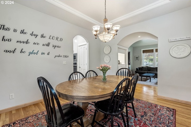 dining space featuring hardwood / wood-style flooring, ornamental molding, a tray ceiling, and a chandelier