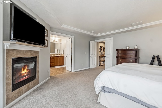 bedroom featuring a tiled fireplace, light carpet, ensuite bathroom, and crown molding