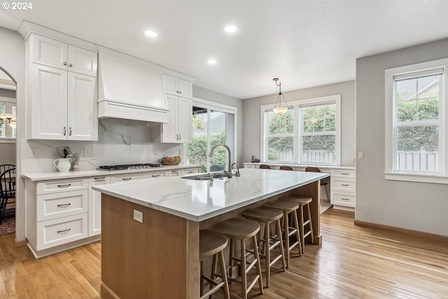 kitchen with a wealth of natural light, custom exhaust hood, a kitchen island with sink, and white cabinetry